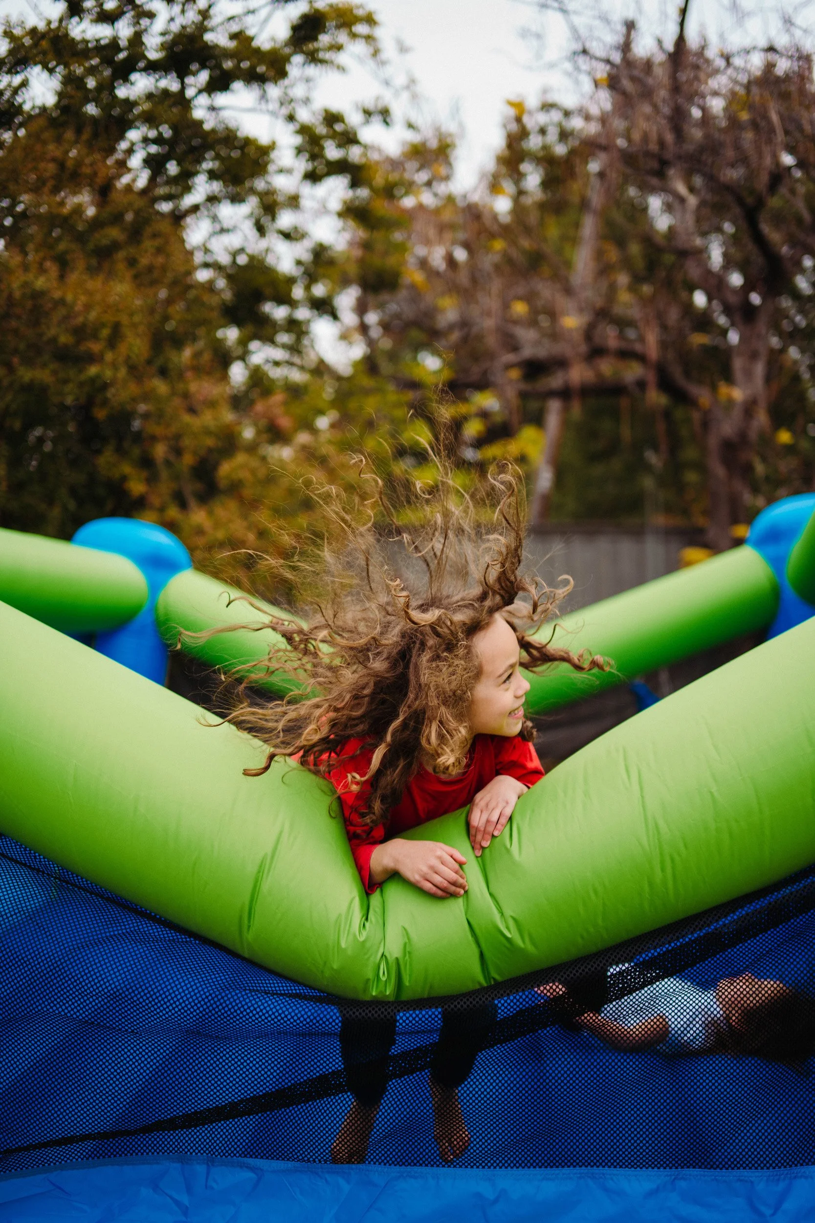 Child with curly hair in a red shirt playing on a green inflatable bounce house.