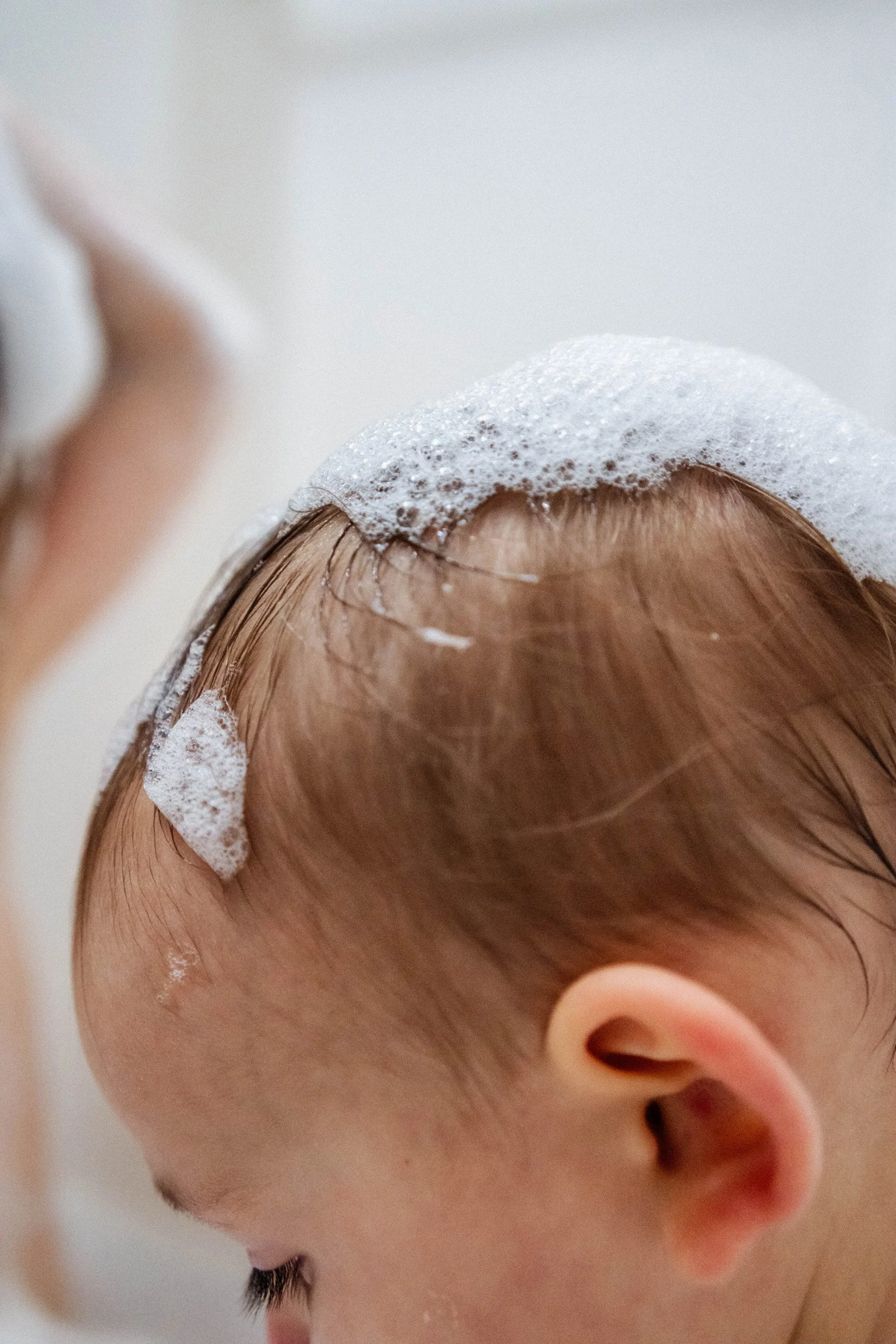 Close-up of a child's head with soap lather on the scalp during a bath.