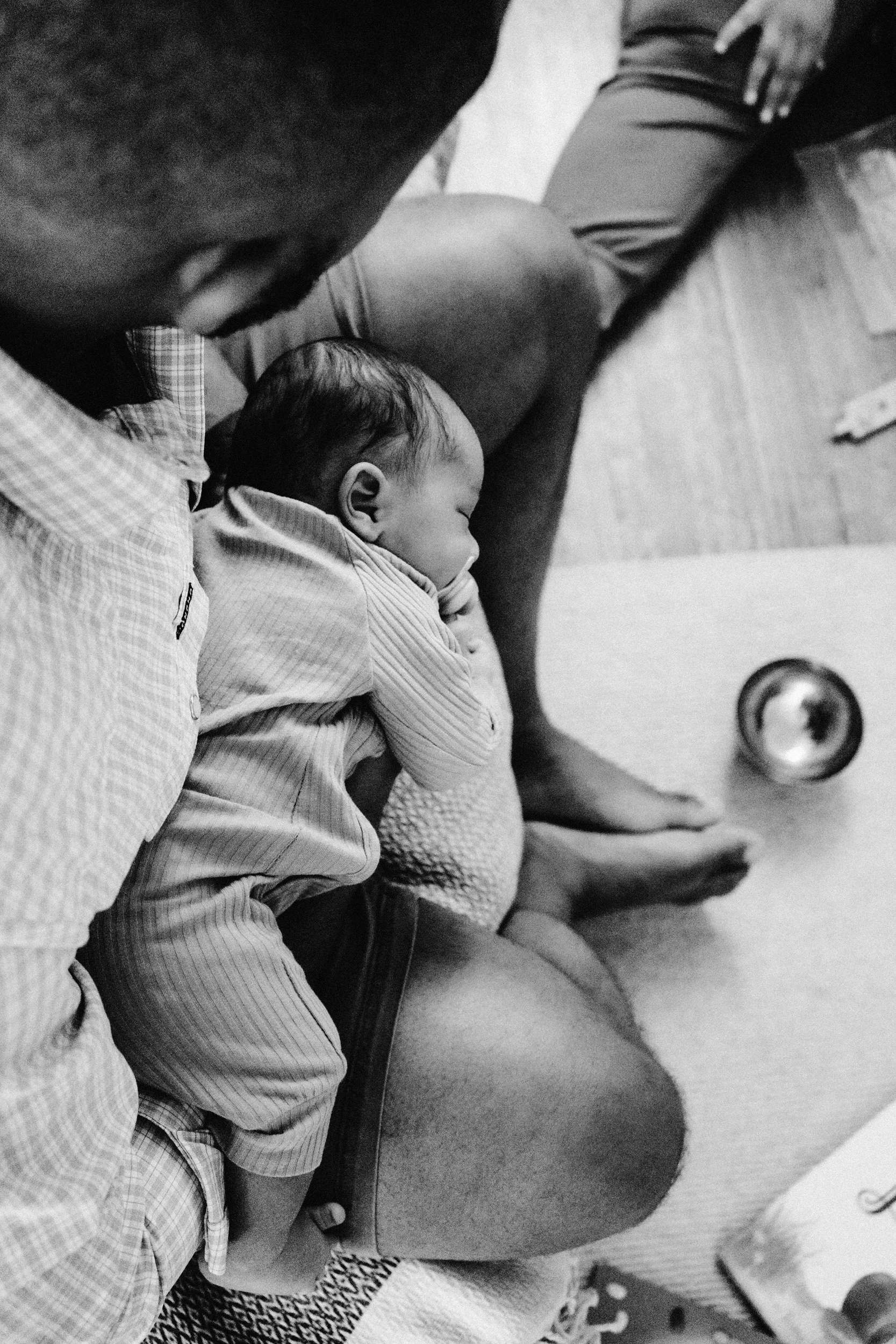 A person and a sleeping baby are sitting on a floor, with the person's hand resting on the baby's head. The scene is in a black-and-white photo.