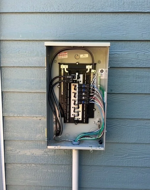 Open electrical breaker box with circuit breakers and wiring mounted on blue wooden wall.