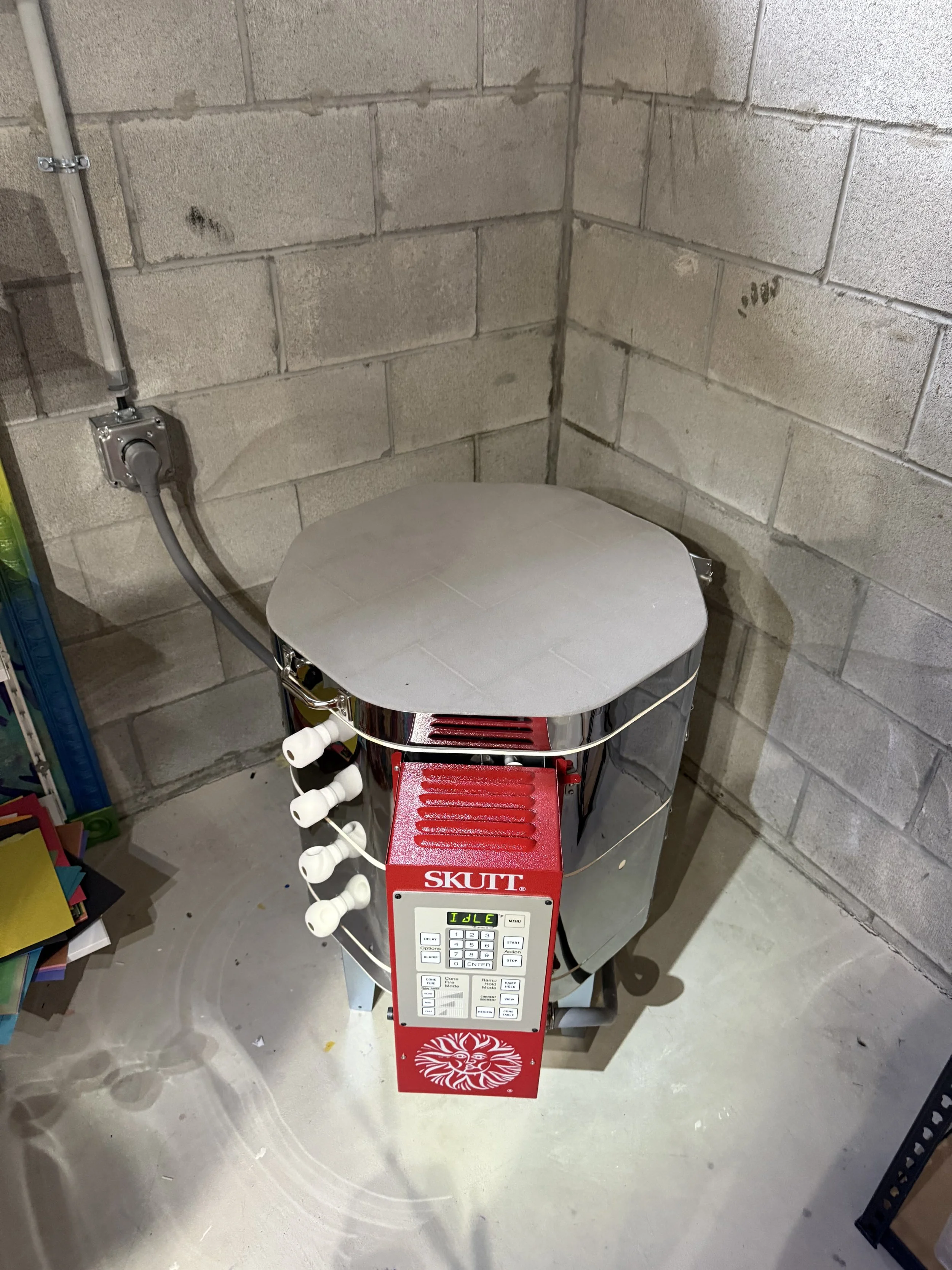A metal ski formation with a digital control panel and a red decorative panel at the bottom, placed on a concrete floor, in a room with cinder block walls and exposed wiring.