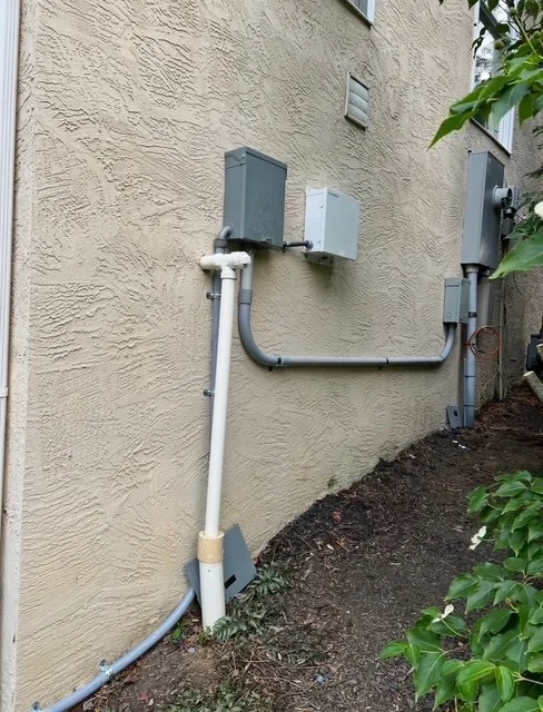 Electrical meters and conduit pipes on the exterior beige wall of a building.