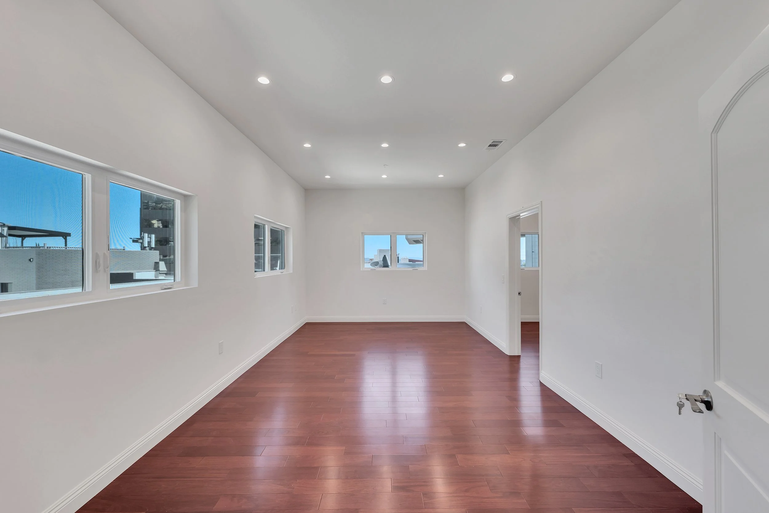 Empty room with white walls, hardwood floors, multiple windows, and a doorway.