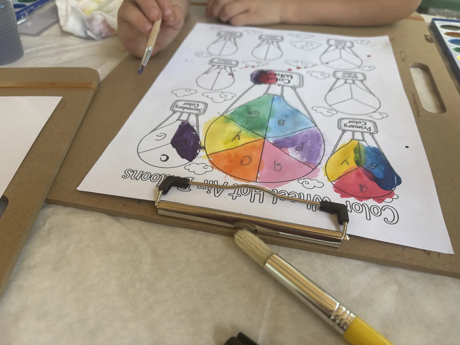 A child painting a color wheel hot air balloon worksheet with watercolors