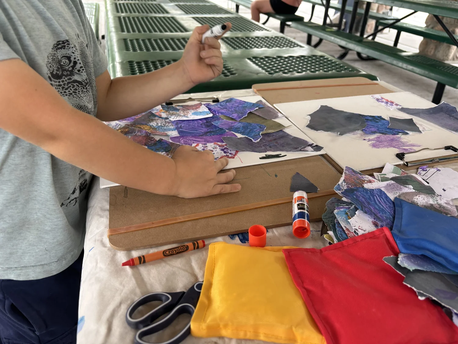 A child assembling a torn-paper collage with glue sticks, scissors and markers