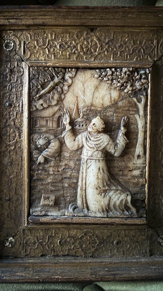 Carved relief of St. Francis kneeling with raised hands, a winged crucifix in the clouds, and a sleeping companion