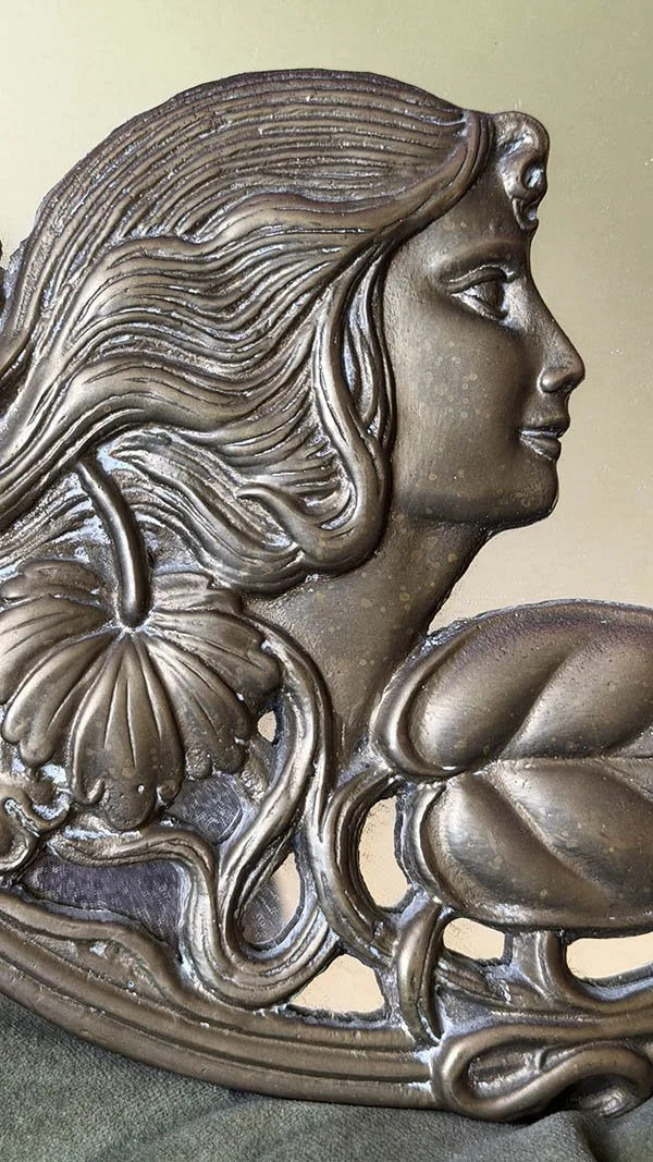 Close-up of a carved maiden's profile and flowing hair on an Art Nouveau brass mirror