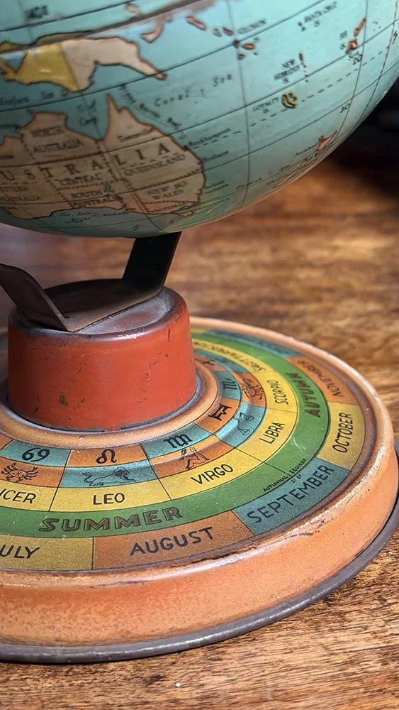 Close detail of a 1930s Ohio Art tin globe showing the lithographed zodiac and seasonal base with a worn brass meridian mount