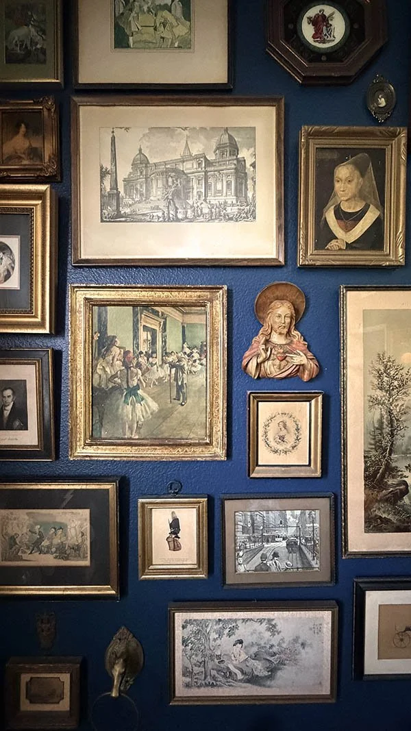 A completed antique frame gallery wall combining mixed frames and one unframed devotional plaque on navy walls