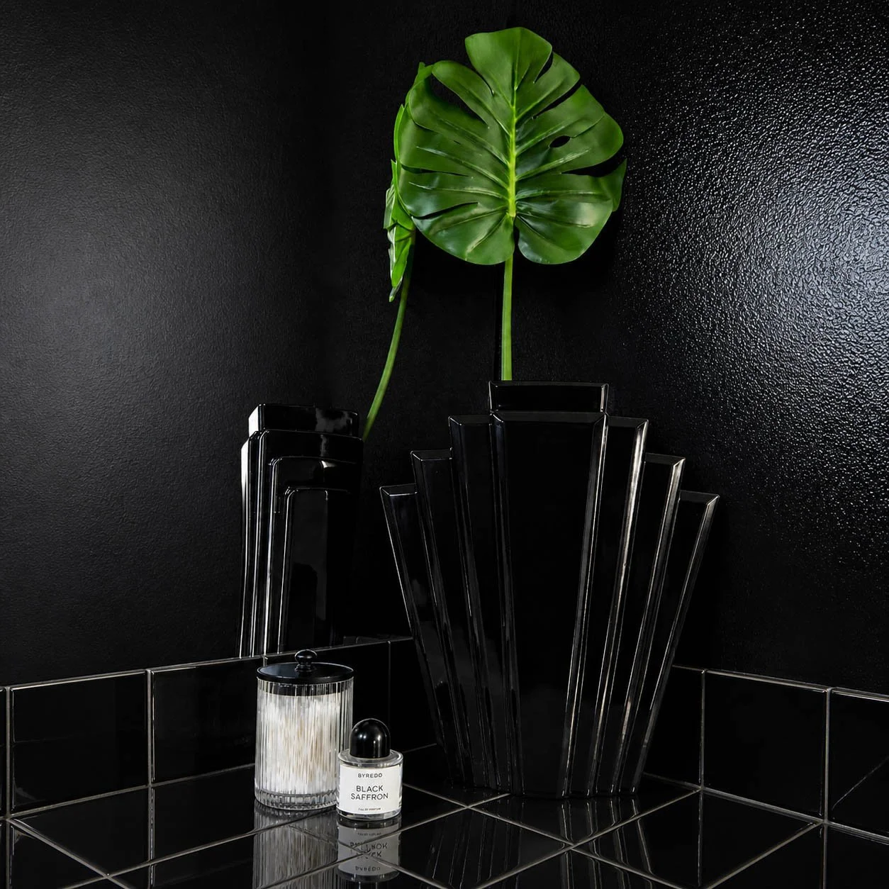 Black fan vase with monstera leaf on black tile bathroom counter, 1980s postmodern glam