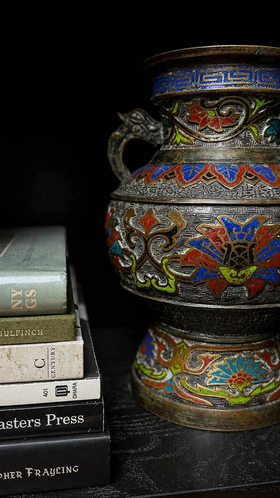 Antique cloisonne urn with dragon handle styled beside a stack of vintage books