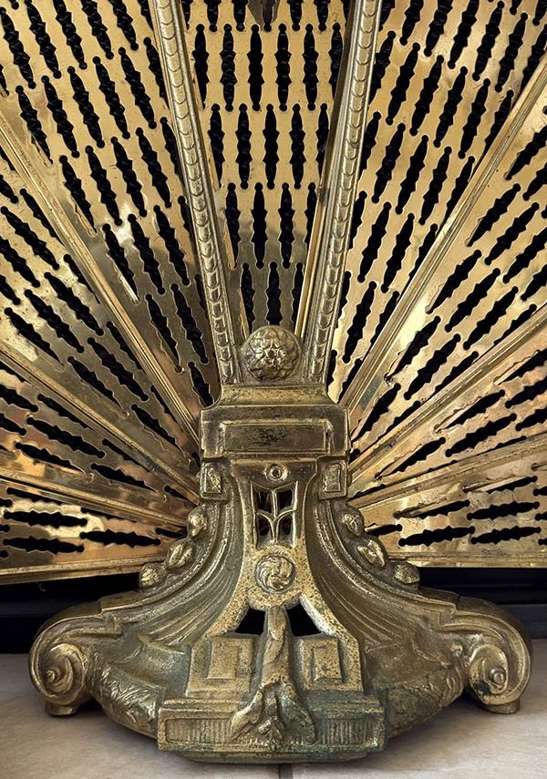 Detail of cast brass acanthus scrollwork and medallion at the base of an antique peacock fireplace screen