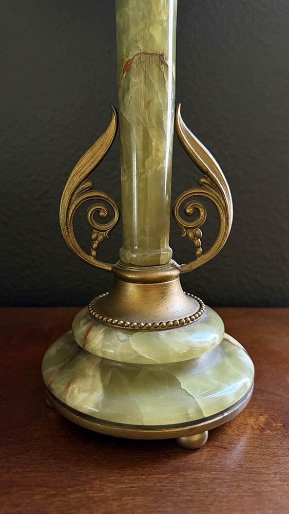 Close-up of a green onyx lamp base with rust-colored veining, brass-colored scrolls, and a beaded collar