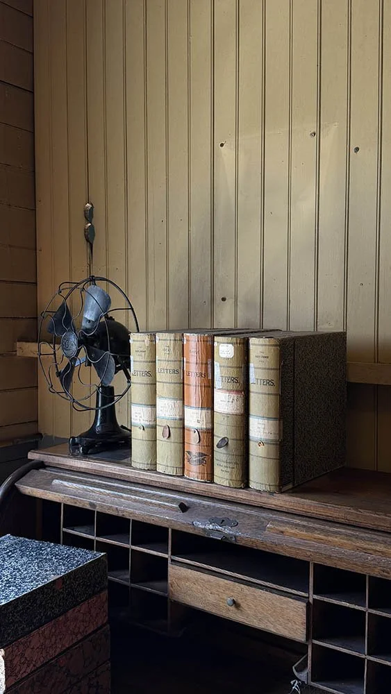 The small black desk fan next to a row of worn canvas ledgers labeled "Letters"