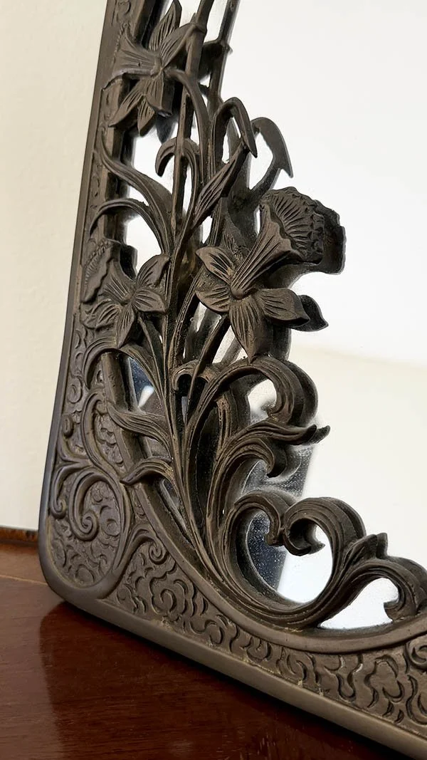 Close-up of carved daffodil and scrollwork detail on an antique brass mirror frame