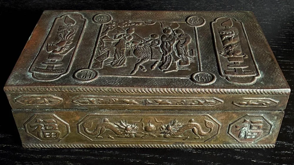 Antique Chinese decorative metal box with relief dragon and figural motifs on a dark shelf