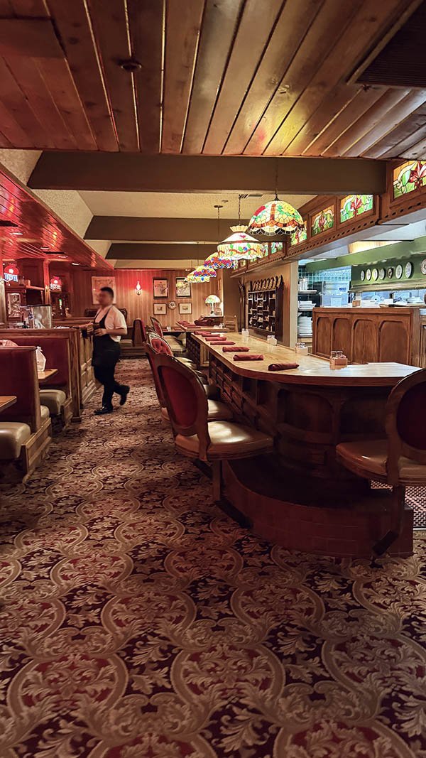 Curved wood bar with stained glass Tiffany-style lamps and red velvet chairs at Billy Reed's restaurant in Palm Springs