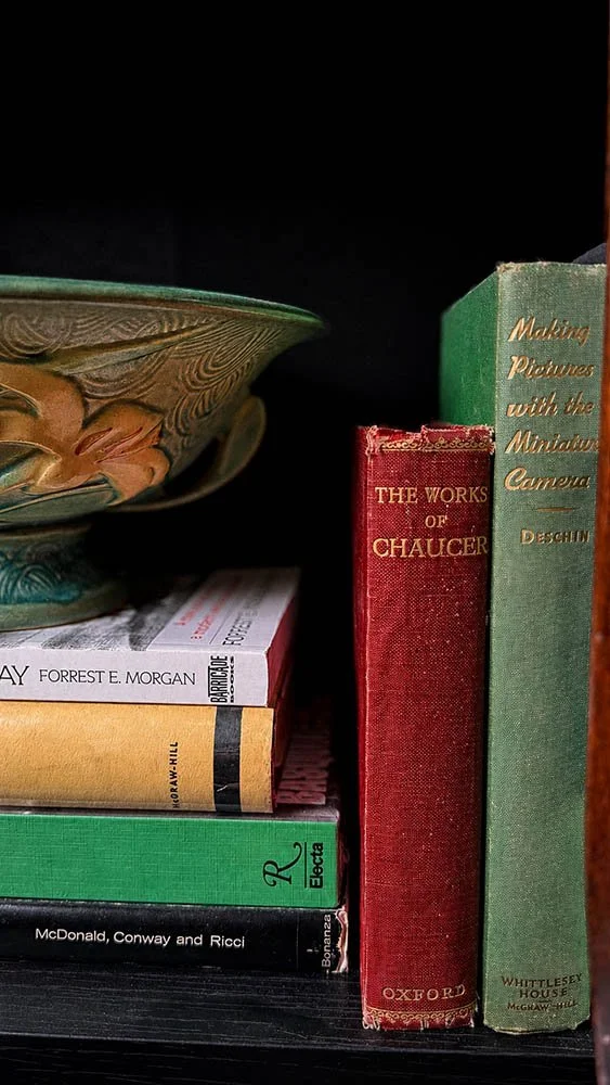Vintage book stack on a dark academia bookshelf topped with a green art pottery bowl