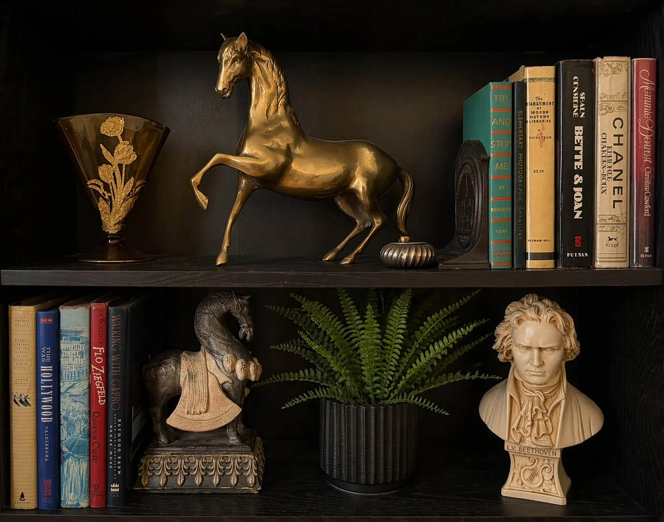 Two-shelf dark bookcase styled with a brass rearing horse sculpture, Beethoven bust, fern, Art Deco fan vase and vintage hardcover books