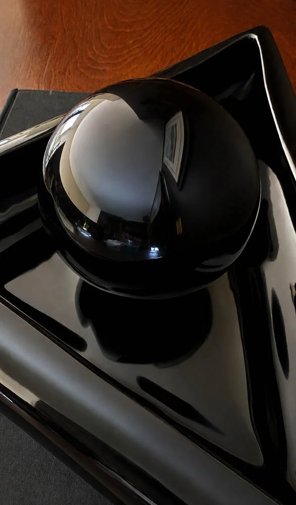 Close detail of a glossy black sphere sitting in a black lacquer triangular dish, postmodern glam styling