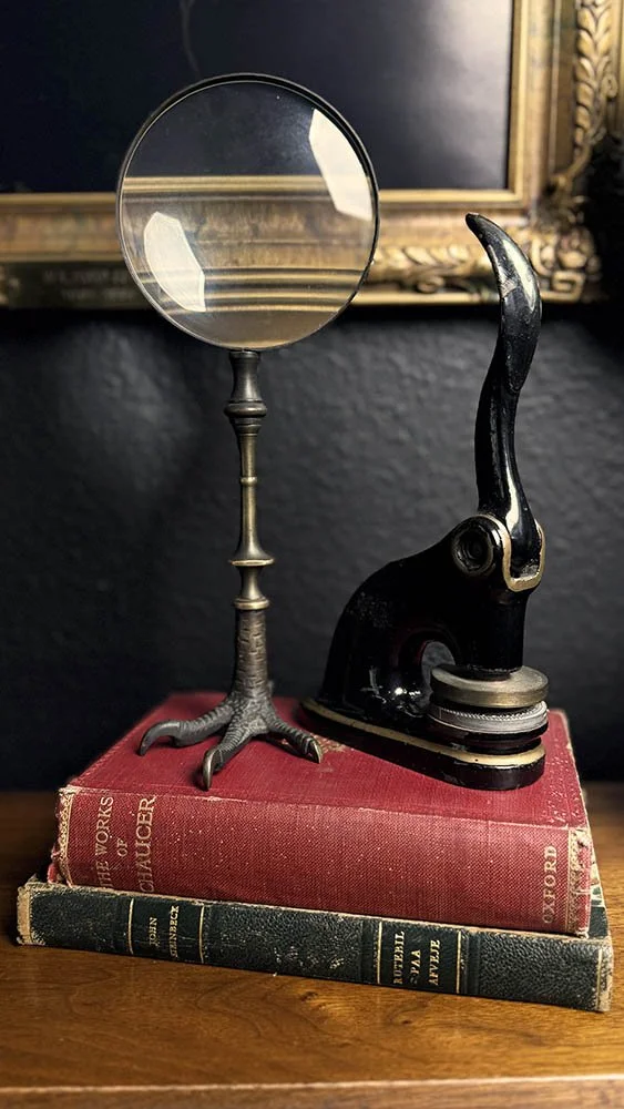 A brass-handled magnifying glass and black embossing seal resting on a stack of antique cloth-bound books