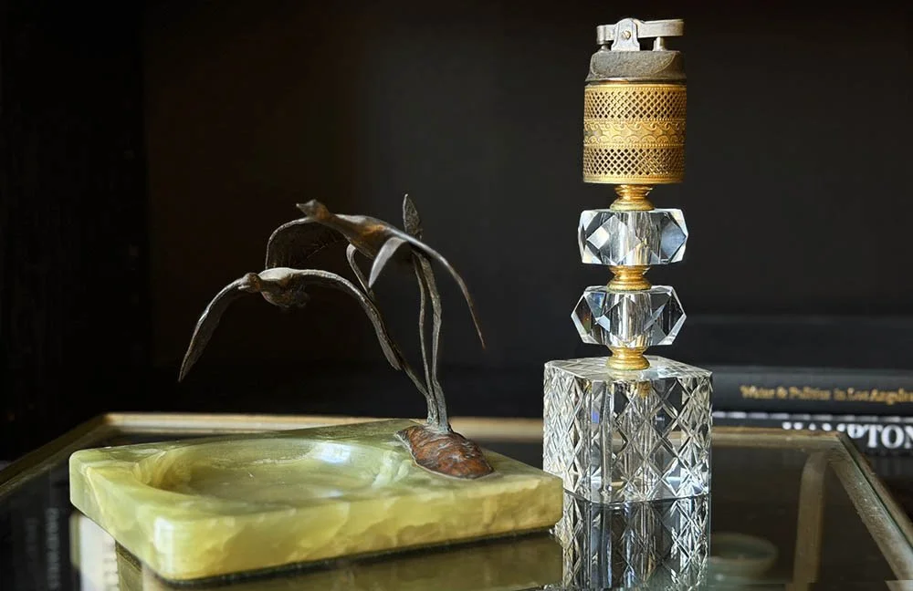 Crystal and brass table lighter beside a green onyx ashtray with two metal birds in flight
