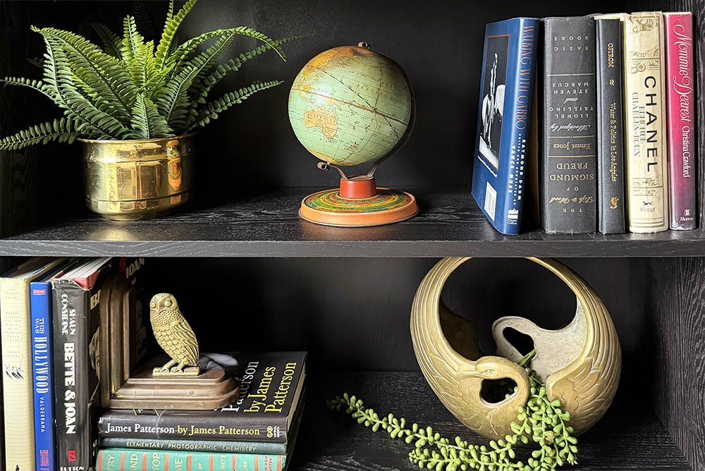 1930s Ohio Art globe styled on a dark bookshelf with a brass planter, fern, and stacked vintage books