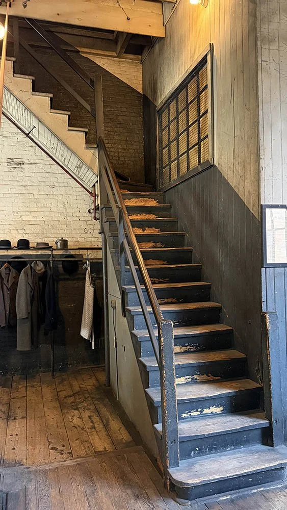 Worn wooden staircase with vintage coats and hats hanging beside it inside Edison's laboratory