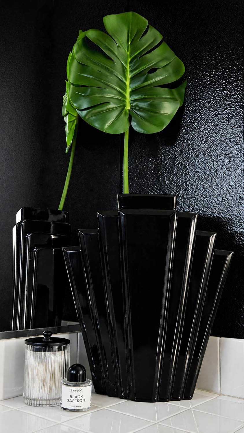 Sculptural black lacquer vessels and a monstera leaf styled against a black wall in the Black Lacquer collection