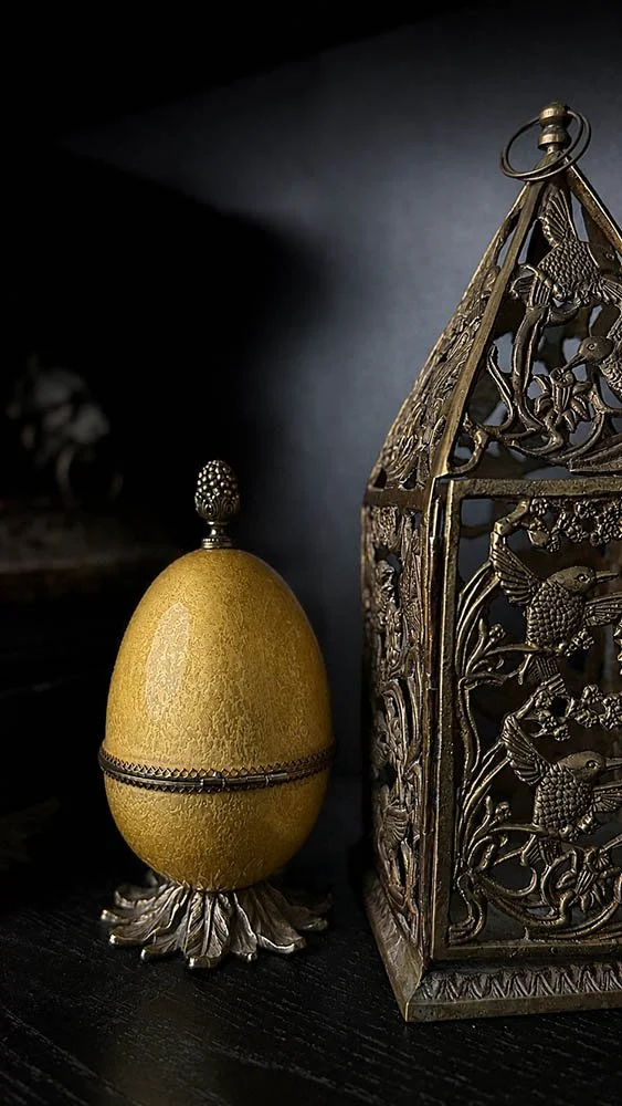 Brass filigree lantern beside a vintage egg box on a dark study bookshelf