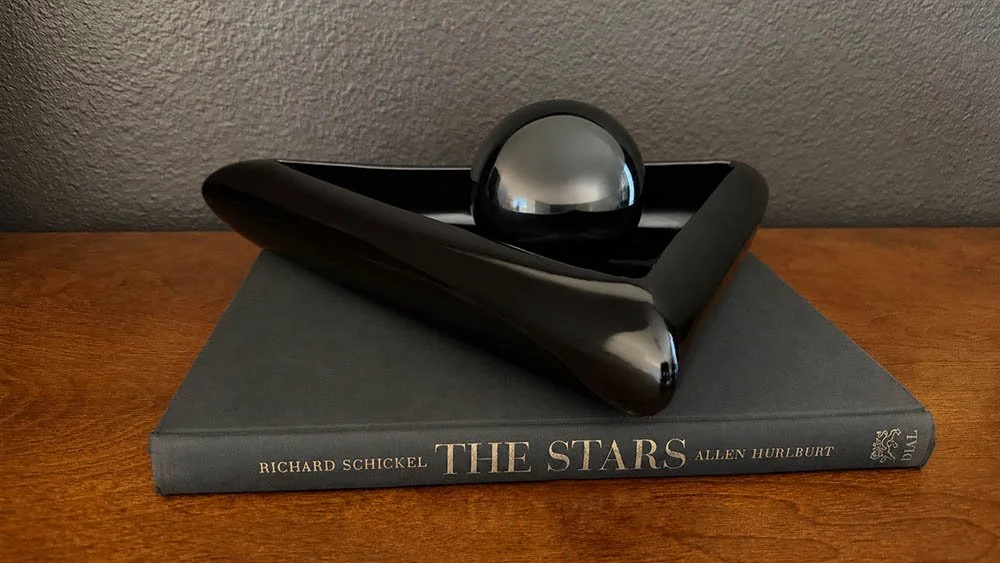 Black lacquer triangular dish with a glossy black sphere resting inside, 80s postmodern decor styling