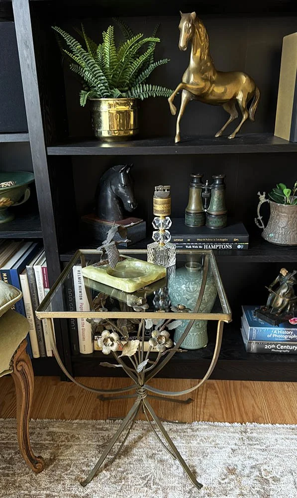 Crystal table lighter and onyx ashtray on a small gold table in front of a dark bookshelf