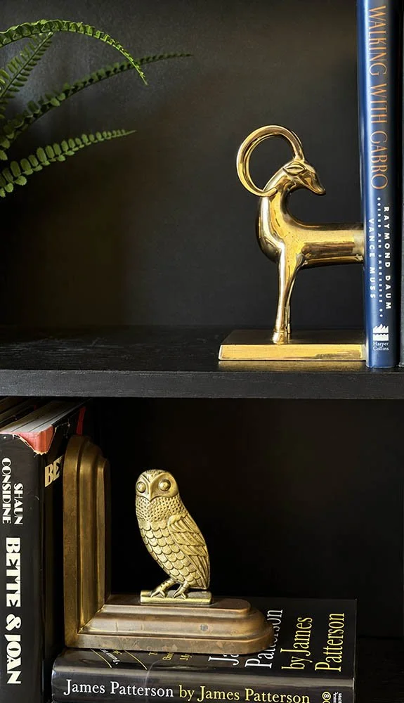 Brass ibex bookend and brass owl bookend displayed separately across two dark bookshelves