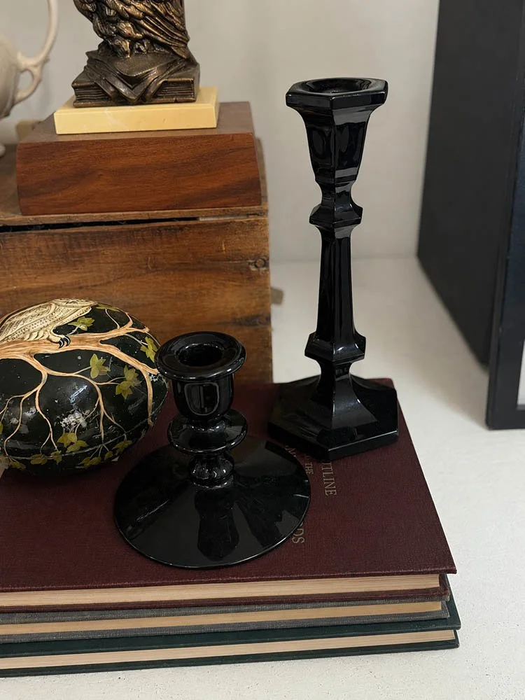 Black lacquer candlesticks styled on a stack of books beside a carved black object.