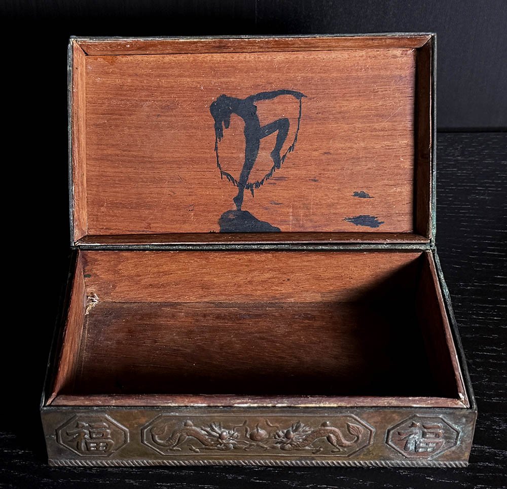 Interior of antique metal box showing a painted Art Deco figure inside the lid