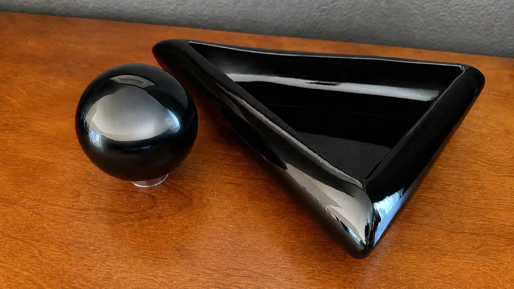 A black glass sphere and black lacquer triangular dish sitting separately before styling, 80s postmodern glam objects