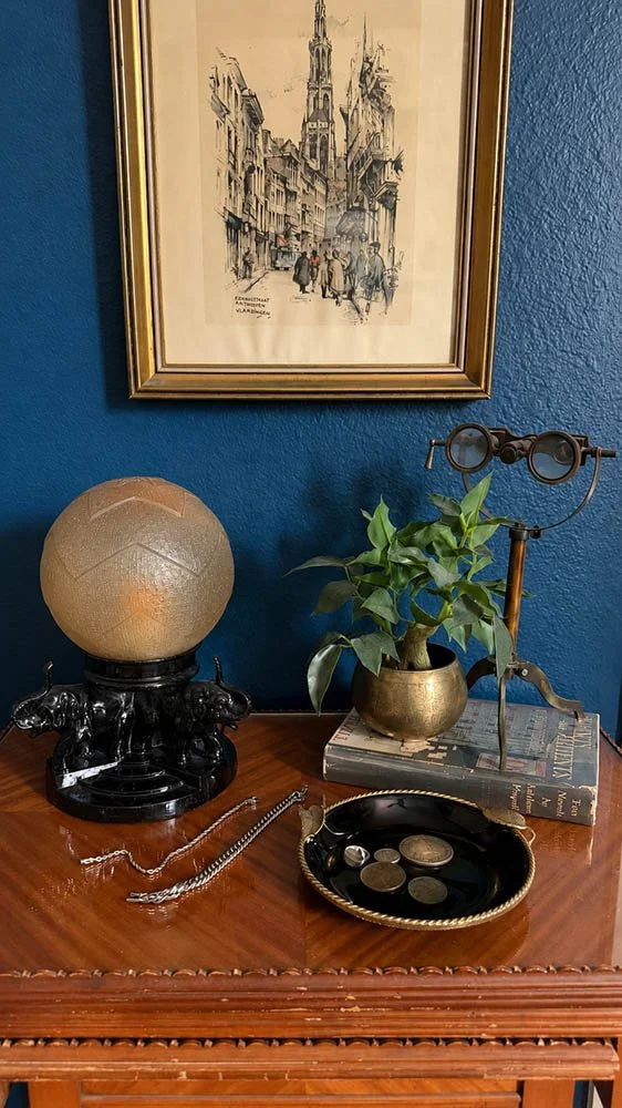 Antique nesting table styled with a glass globe lamp, brass planter, and opera glasses on a dark wood surface