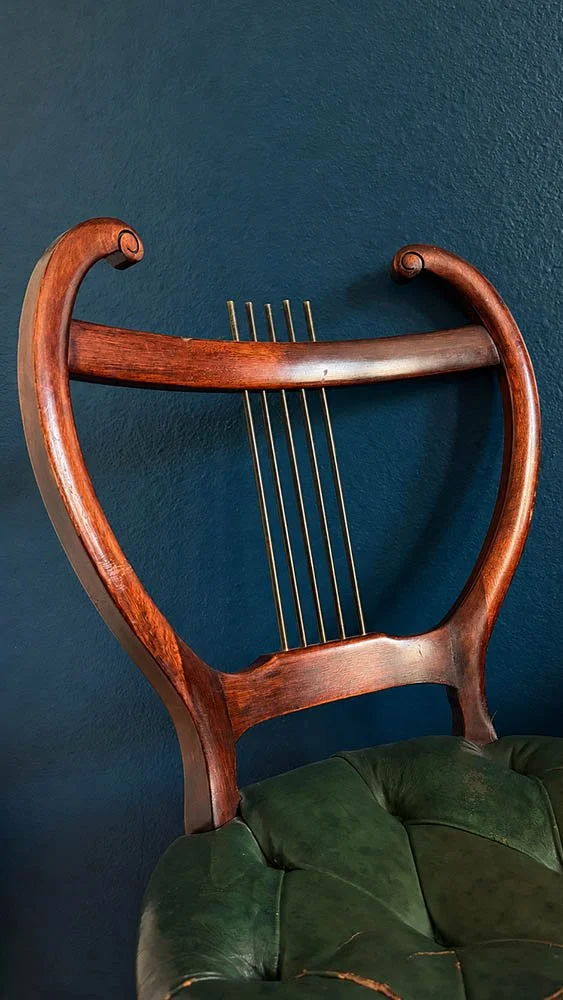 Detail of a mahogany lyre back chair with worn green leather seat and brass rod detailing
