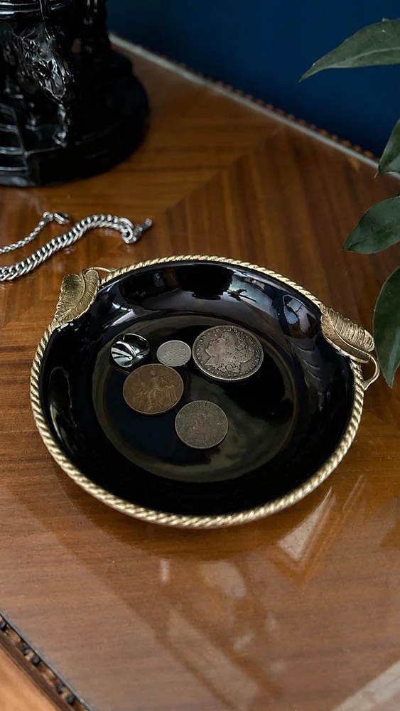 Black rope edge dish holding a silver ring and antique coins including a 1921 Morgan silver dollar