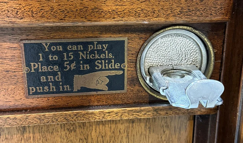 Black and brass plaque with an engraved pointing hand on a Mills Violano-Virtuoso cabinet, reading You can play 1 to 15 nickels.