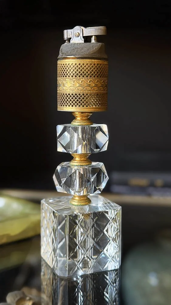 Cut crystal and brass table lighter with a pierced brass sleeve on a glass table in front of dark shelves