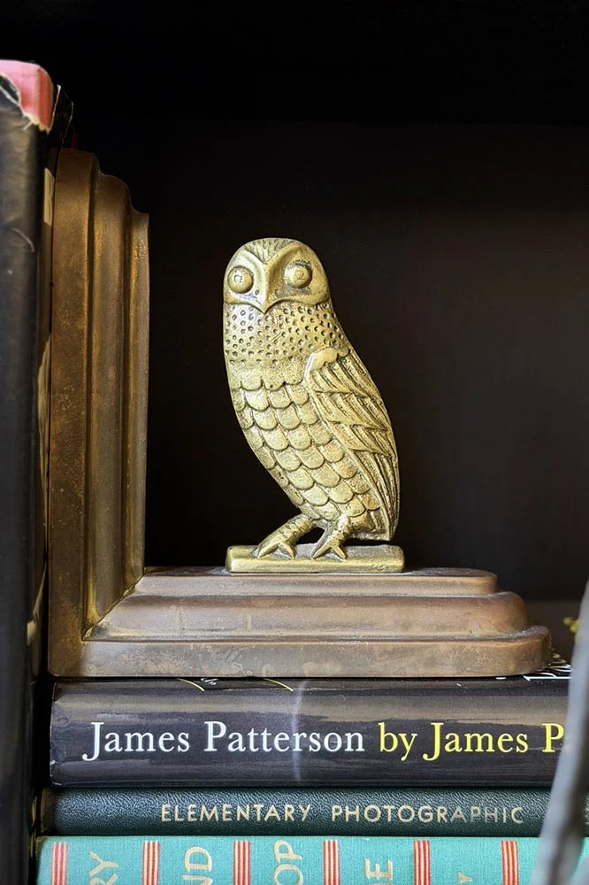 Brass owl bookend with detailed feather casting standing alone on a stack of vintage books