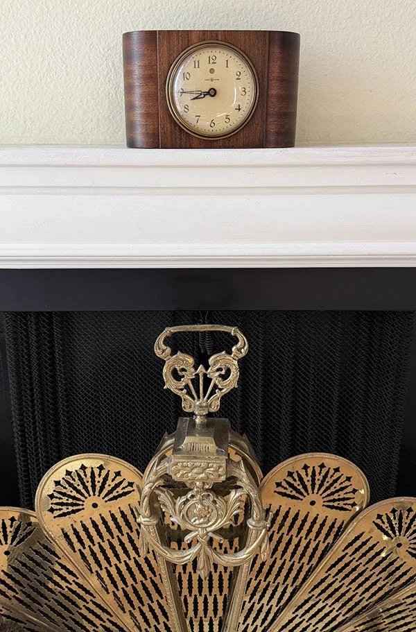 Brass peacock fireplace screen styled with a vintage electric mantel clock on a black and white fireplace