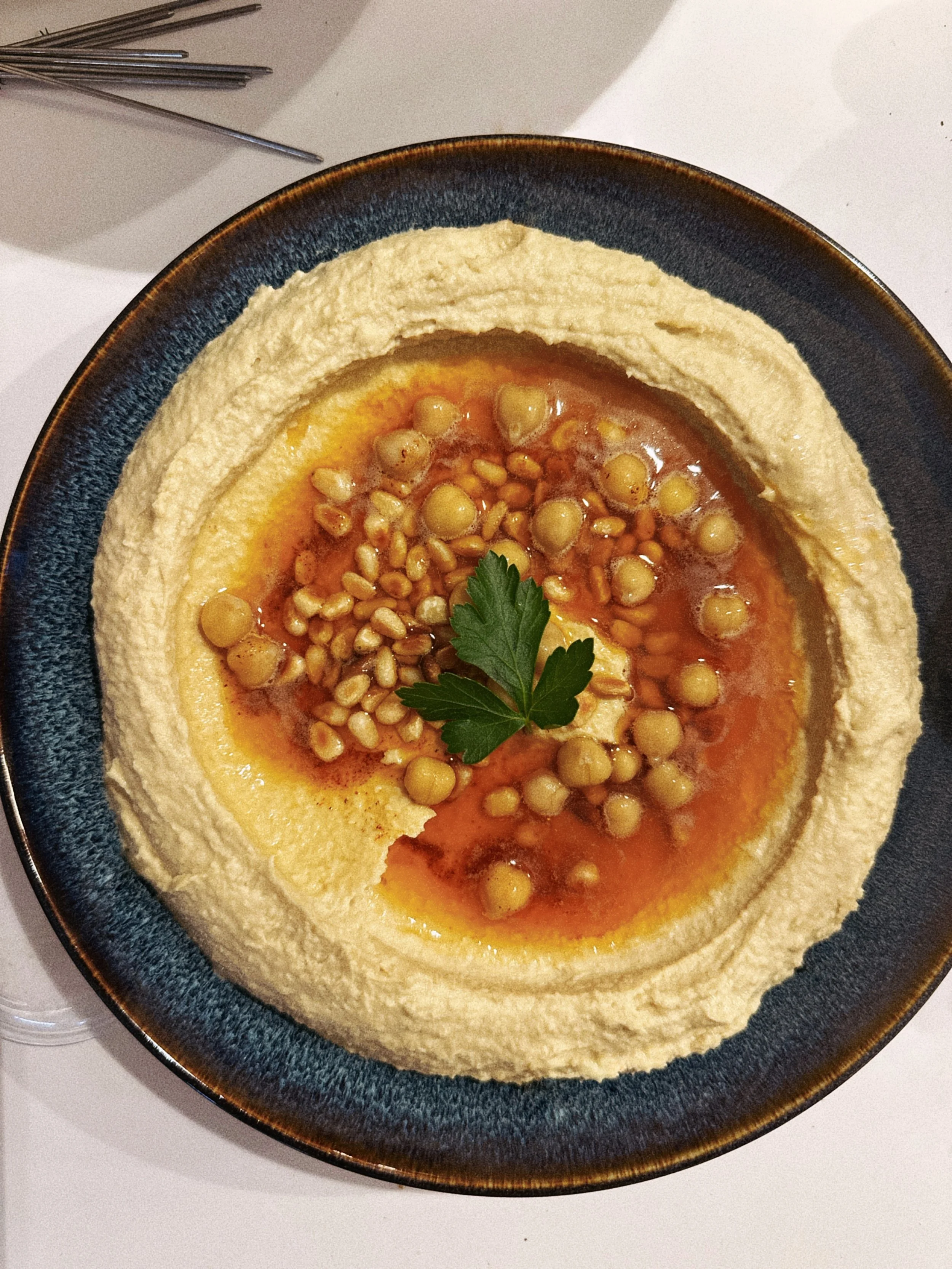 Assiette de houmous garni de pois chiches, de beurre noisette, avec une branche de persil en décoration.