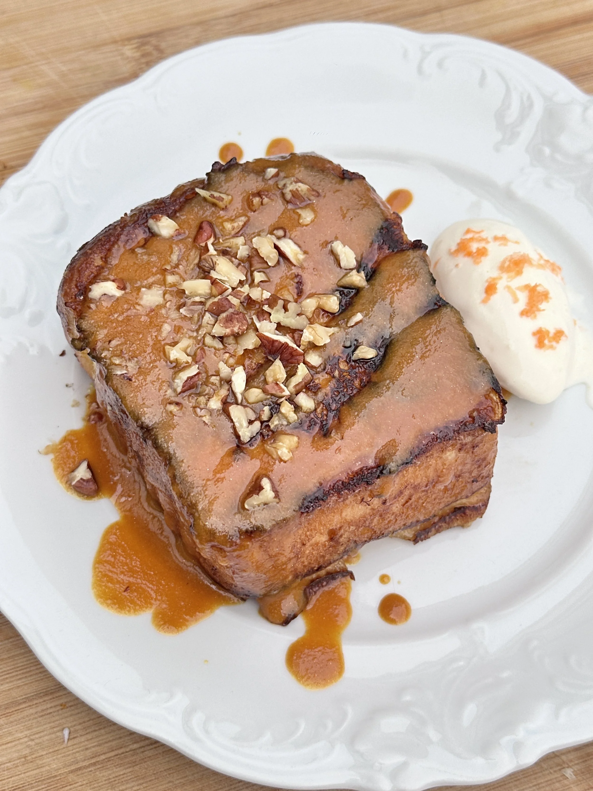 Brioche façon pain perdu avec caramel à la carotte glacé avec des noix hachées, accompagné de crème glacée au yaourt et de sauce caramel sur une assiette blanche