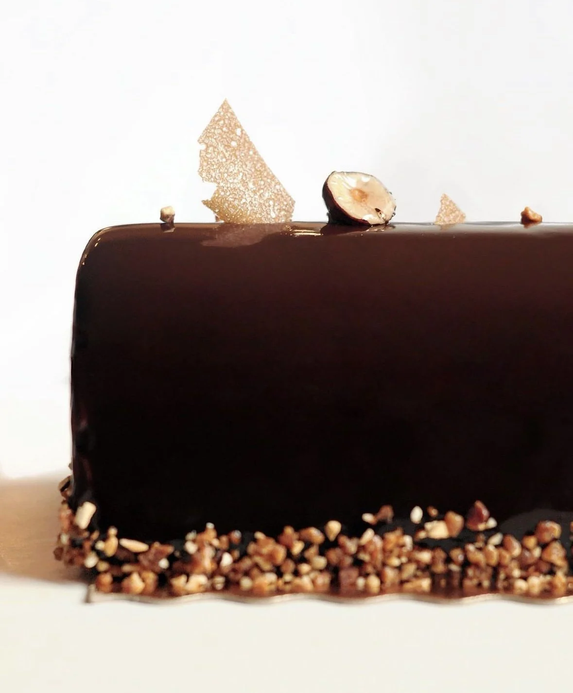 Gâteau au chocolat décoré avec une moitié de noix, des éclats de caramel et des éclats de noisettes ou amandes, avec un fond blanc.