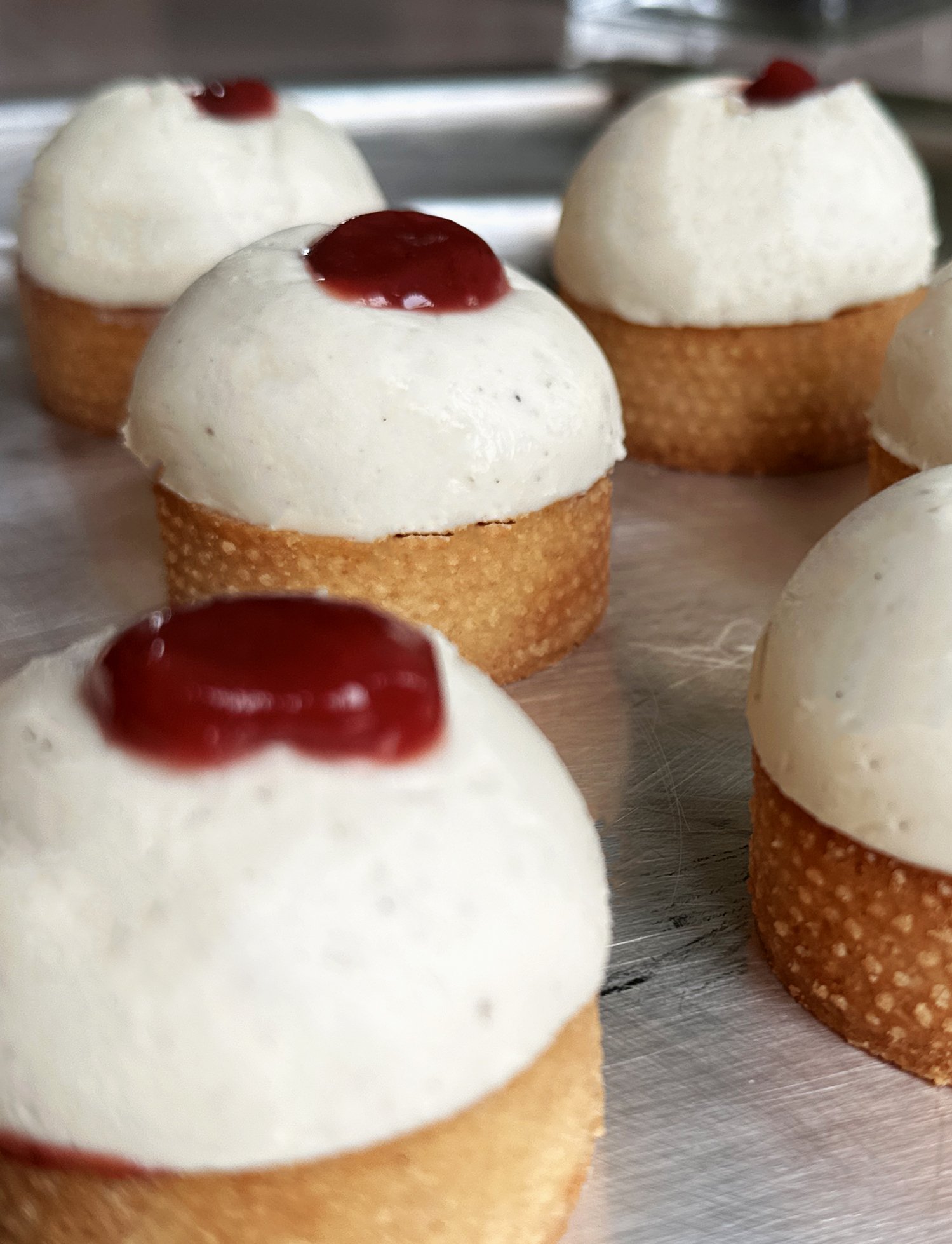 Petites pâtisseries en forme de dôme avec une couche de crème blanche et coulis de fraise rhubarbe en décoration.