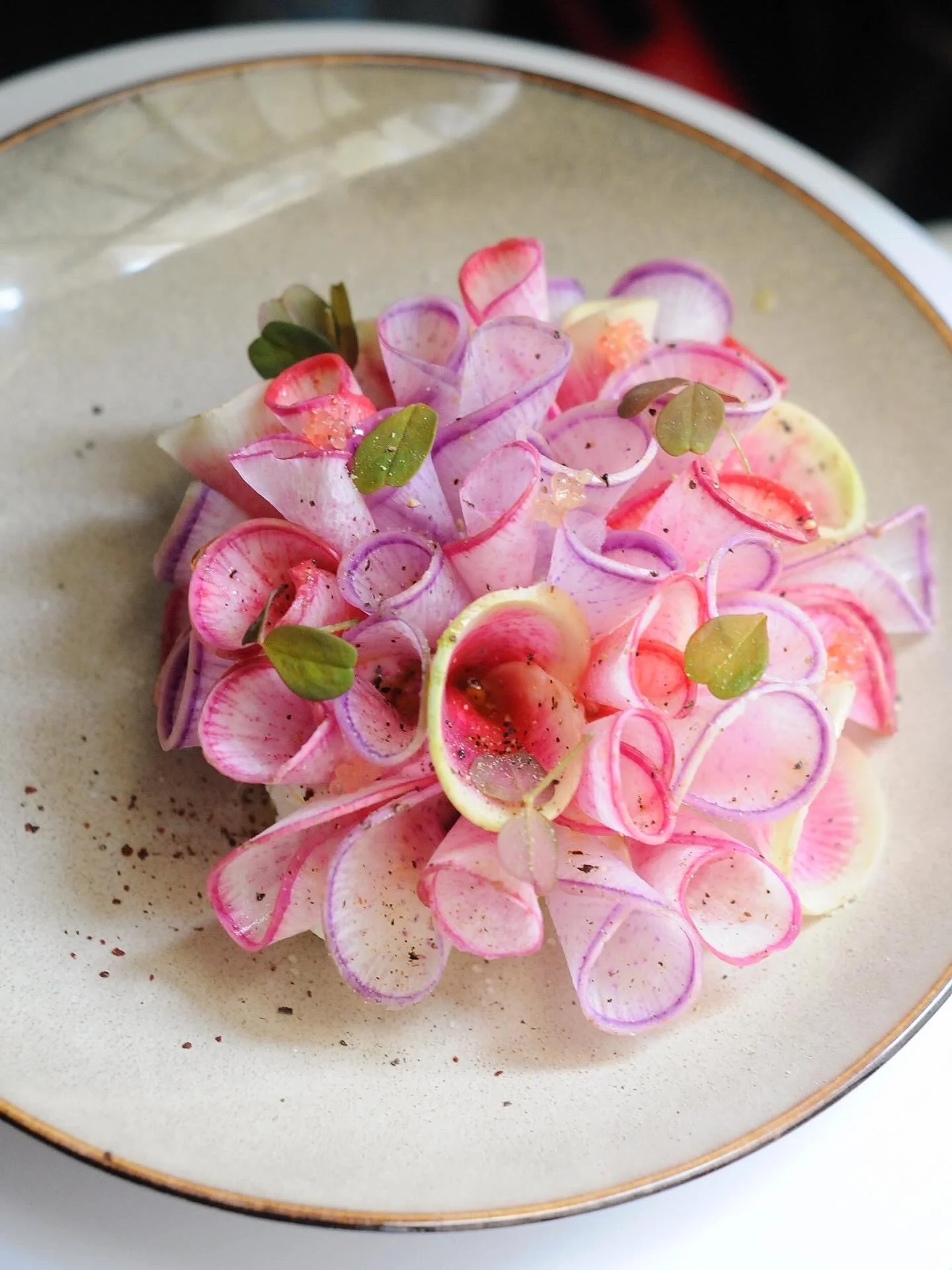 Une assiette de fleurs décoratives faites de fines tranches de radis, avec quelques feuilles vertes, sur un fond clair.