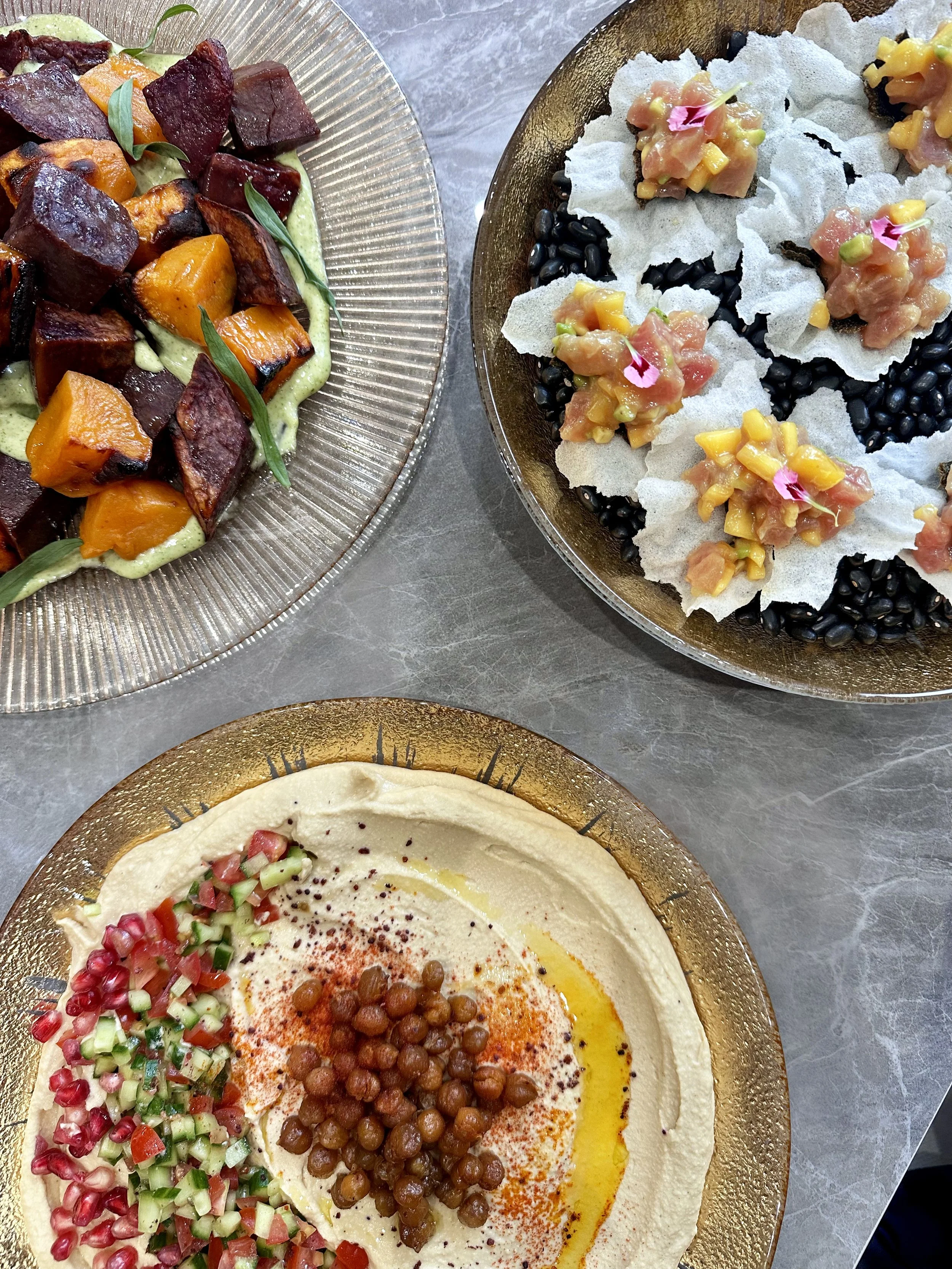 Assiette de houmous avec des garnitures de tomates, concombres, pois chiches et épices, accompagnée d'une autre assiette avec des aliments grillés et des légumes.