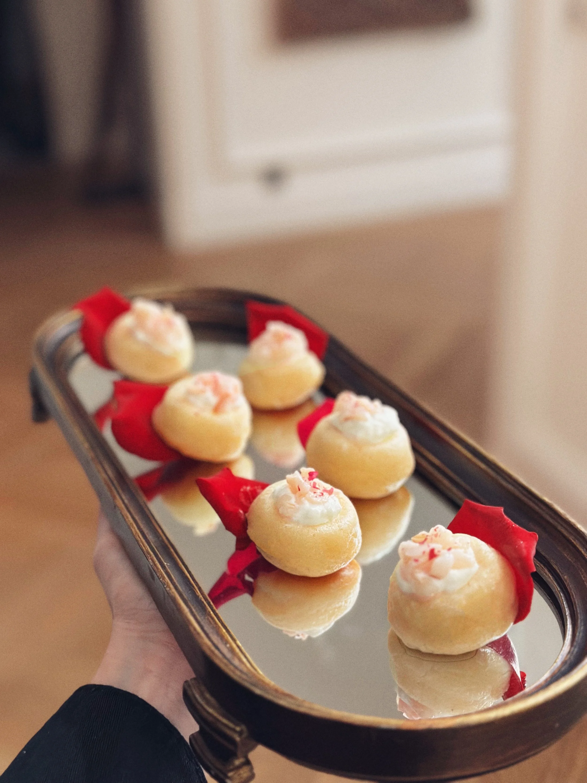 Mini babas au litchi avec chantilly à la rose et pétale de rose servis sur un plateau en bois et miroir